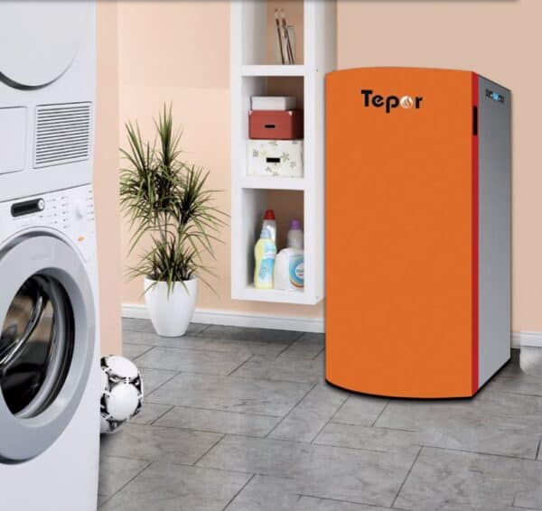 Een CV Pelletketel Tepor Compact 14-32kW in de kleuren oranje en wit staat in een wasruimte met een witte wasmachine, droger, installatie, voetbal, planken met schoonmaakmiddelen en een grijze tegelvloer.